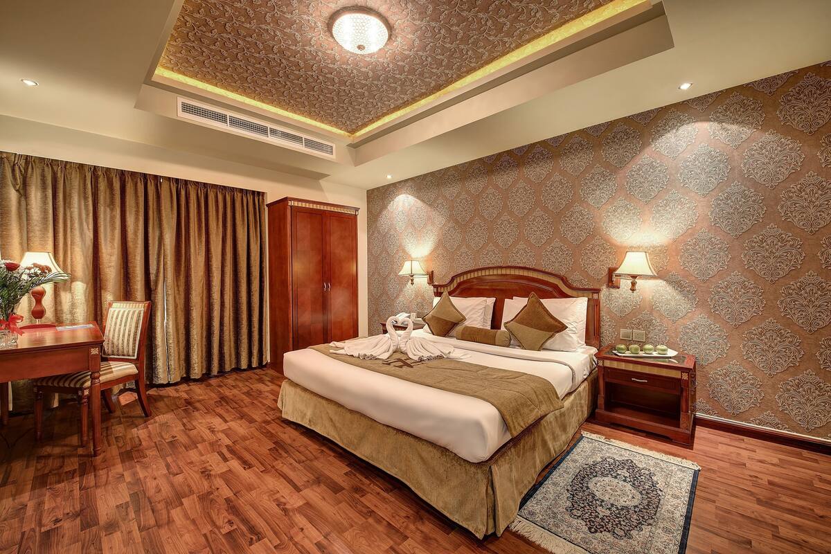 A hotel room with a large bed, wooden floor, a desk with a lamp, and a patterned wall.