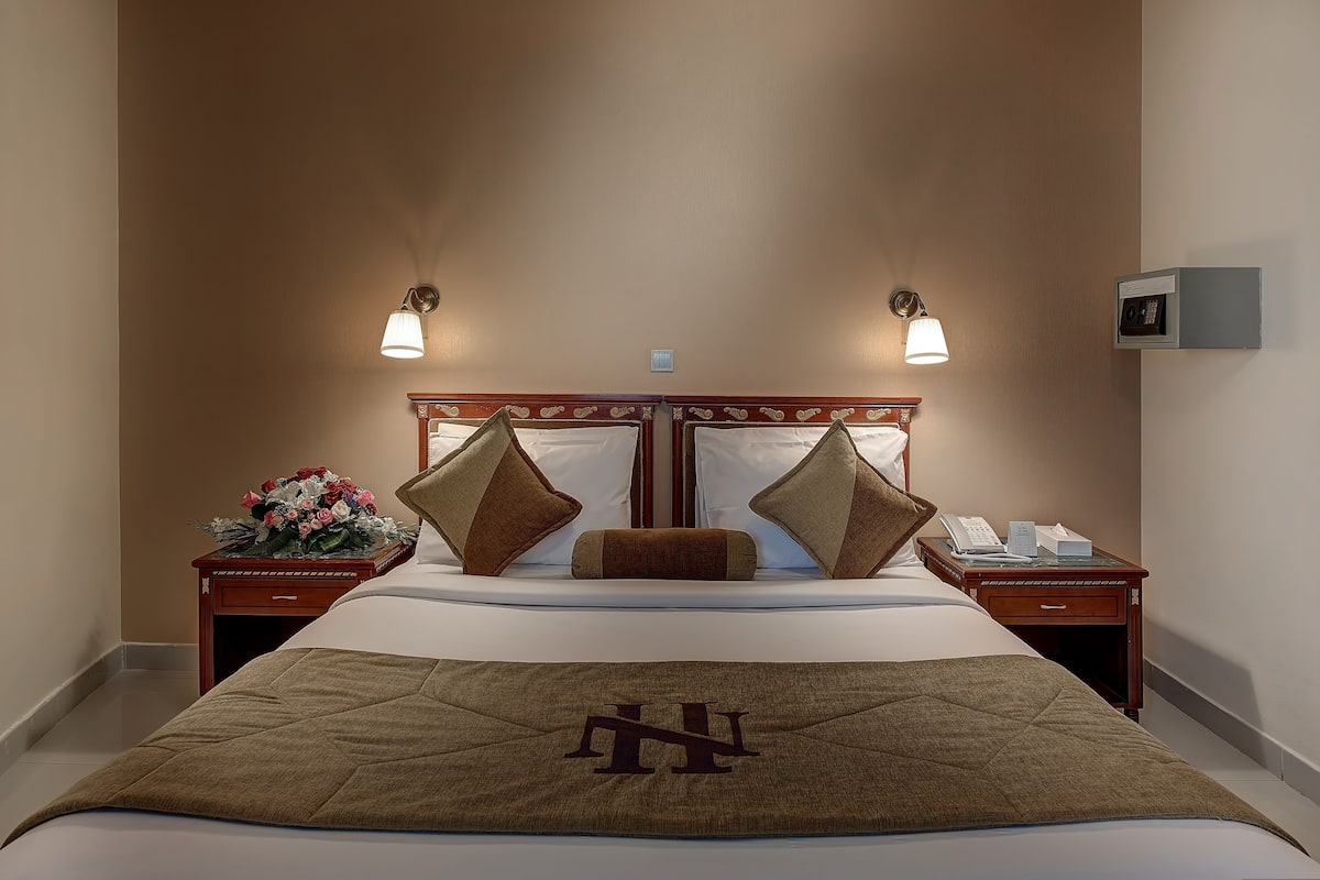 A hotel room with a large bed, two bedside tables, a nightstand with a telephone, and wall-mounted lamps.