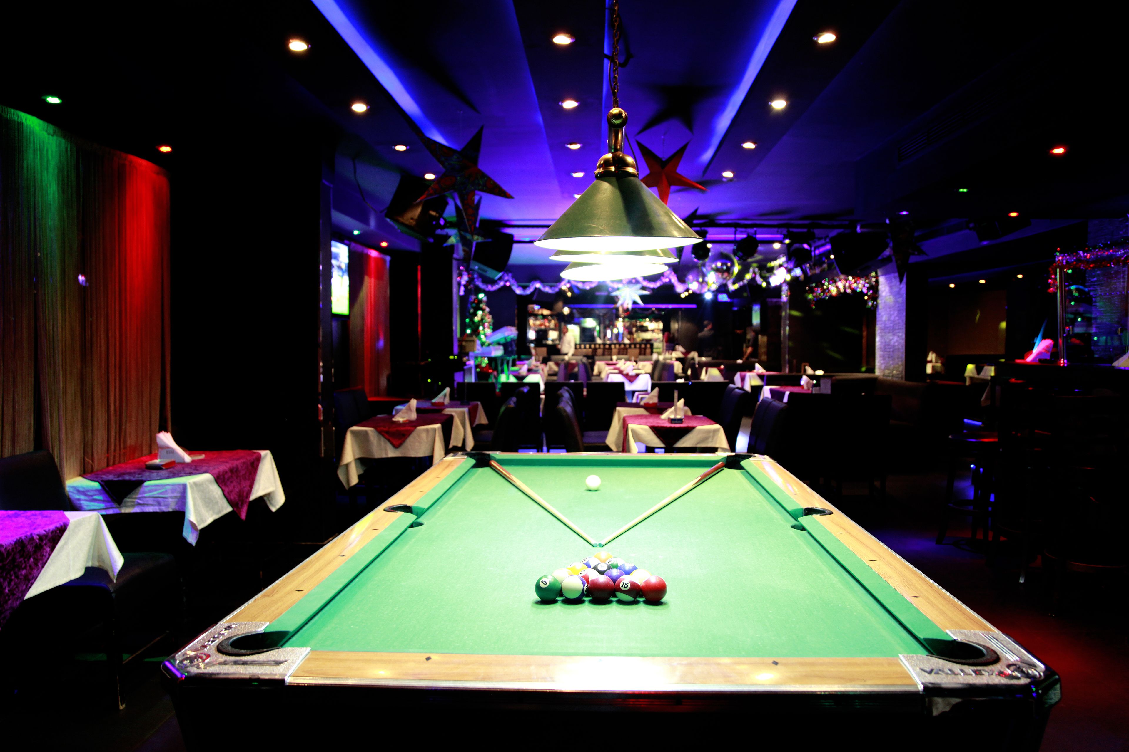 A pool table in a dimly lit room with tables and chairs around it.