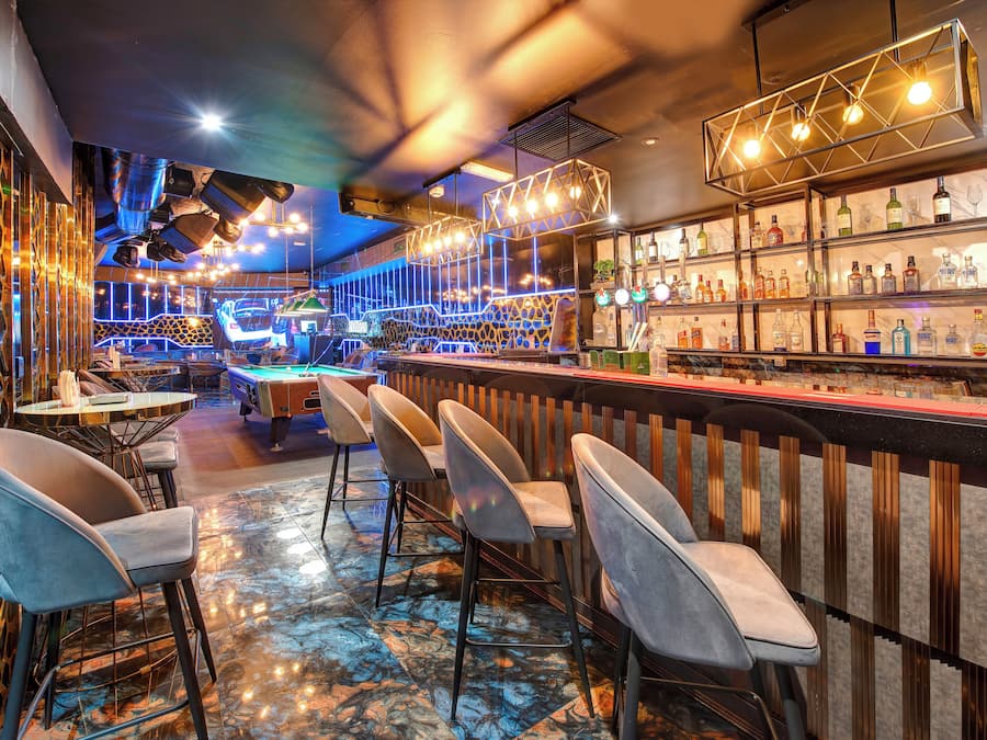 Uma área de bar com diversas opções de assento, uma mesa de bilhar e uma variedade de garrafas nas prateleiras.