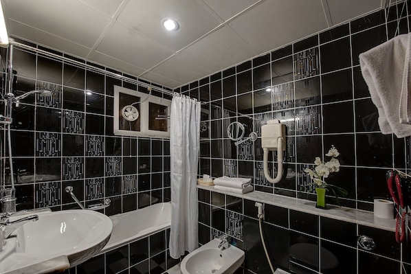 A modern bathroom with black tiled walls, a white sink, a bathtub, and a toilet. - Nihal Hotel (Dubai)