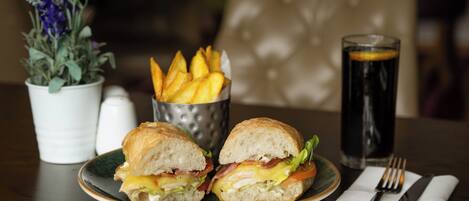 A plate with a sandwich, a glass of soda, and a container of fries on a table.