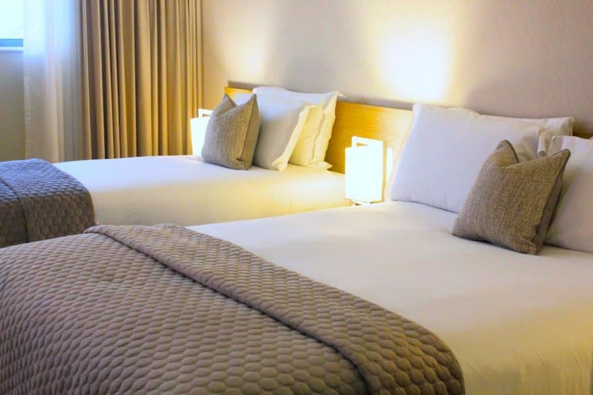 Habitación de hotel con dos camas, cada una con cabecero, almohadas y manta.