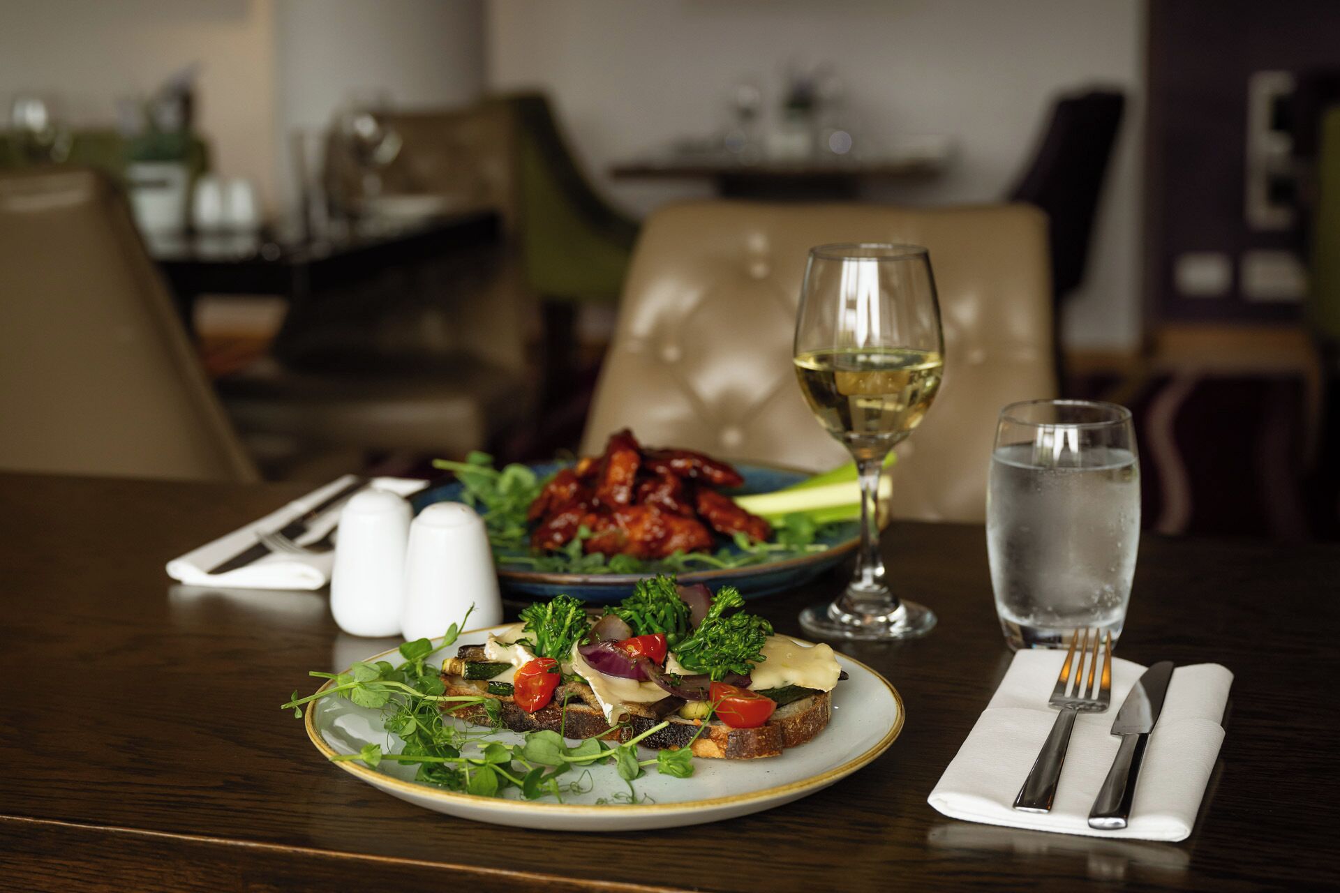A dining table with plates of food, a glass of white wine, and a glass of water.