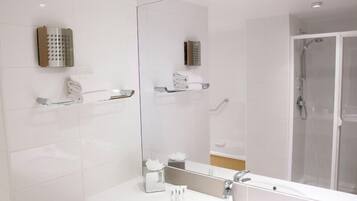 A modern bathroom with a large mirror, white tiles, a shower enclosure, and a vanity with a sink and towel rack.