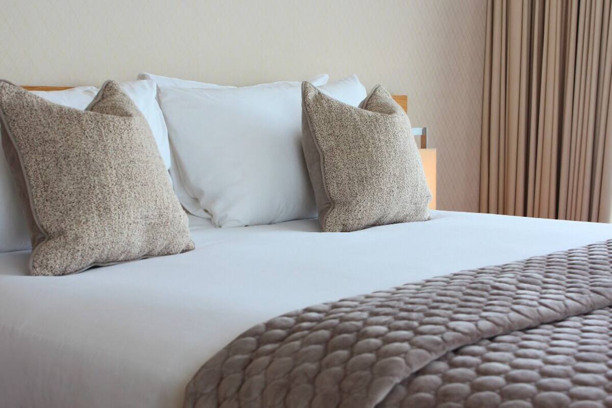 A neatly made bed with white sheets and two beige pillows.