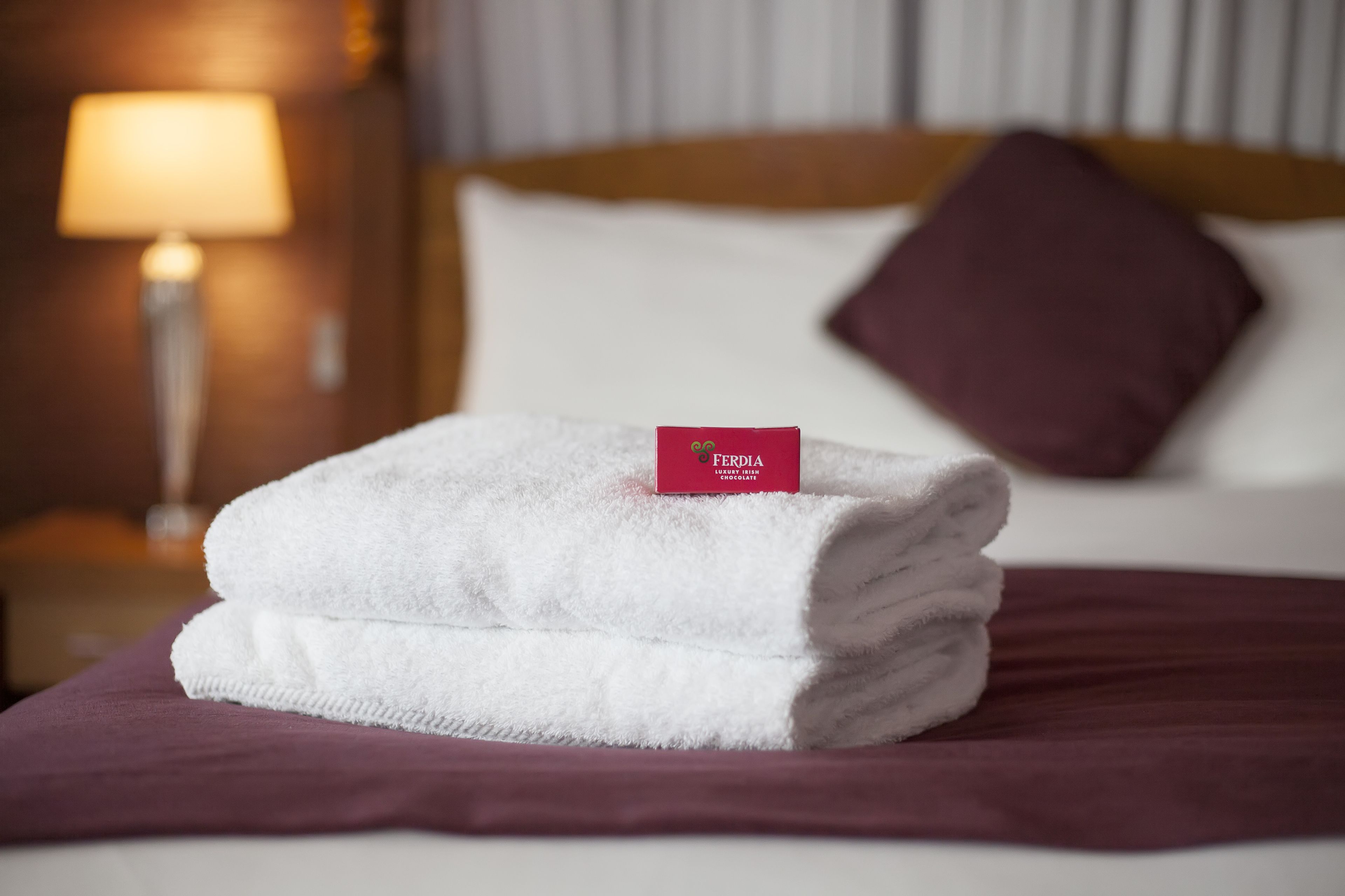 Una toalla blanca doblada con una etiqueta roja sobre una cama con un edredón morado.