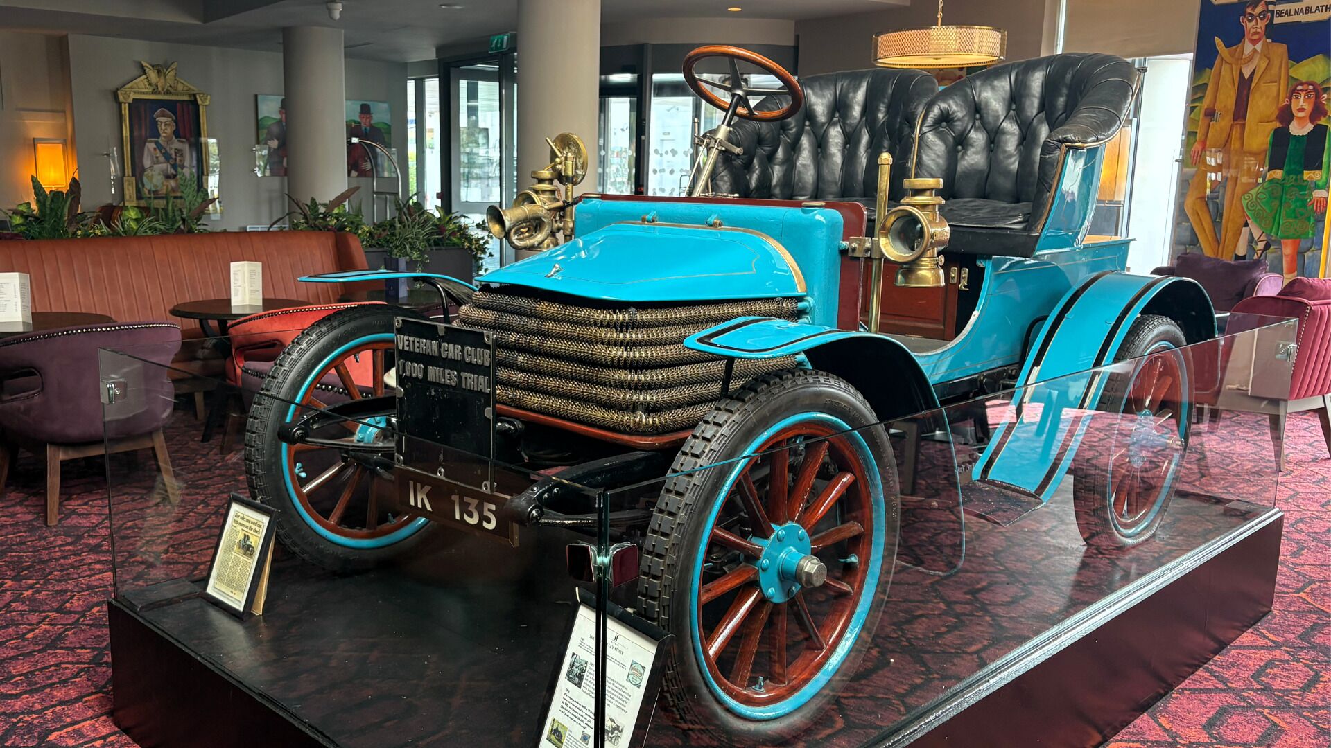 A vintage car on display with a plaque indicating a 1,000 miles trial.