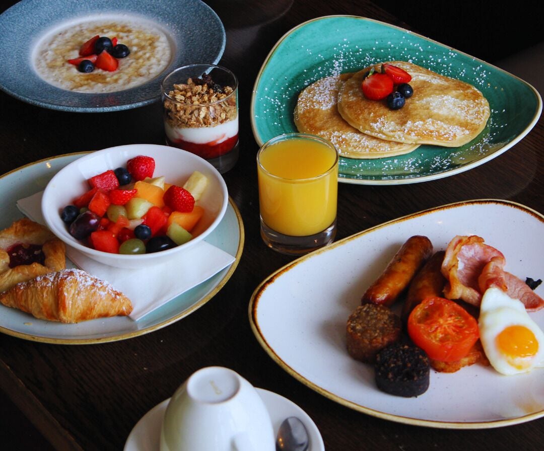 A breakfast table with various dishes including pancakes, sausages, eggs, and a fruit bowl.