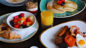 A breakfast table with various dishes including pancakes, sausages, eggs, and a fruit bowl.