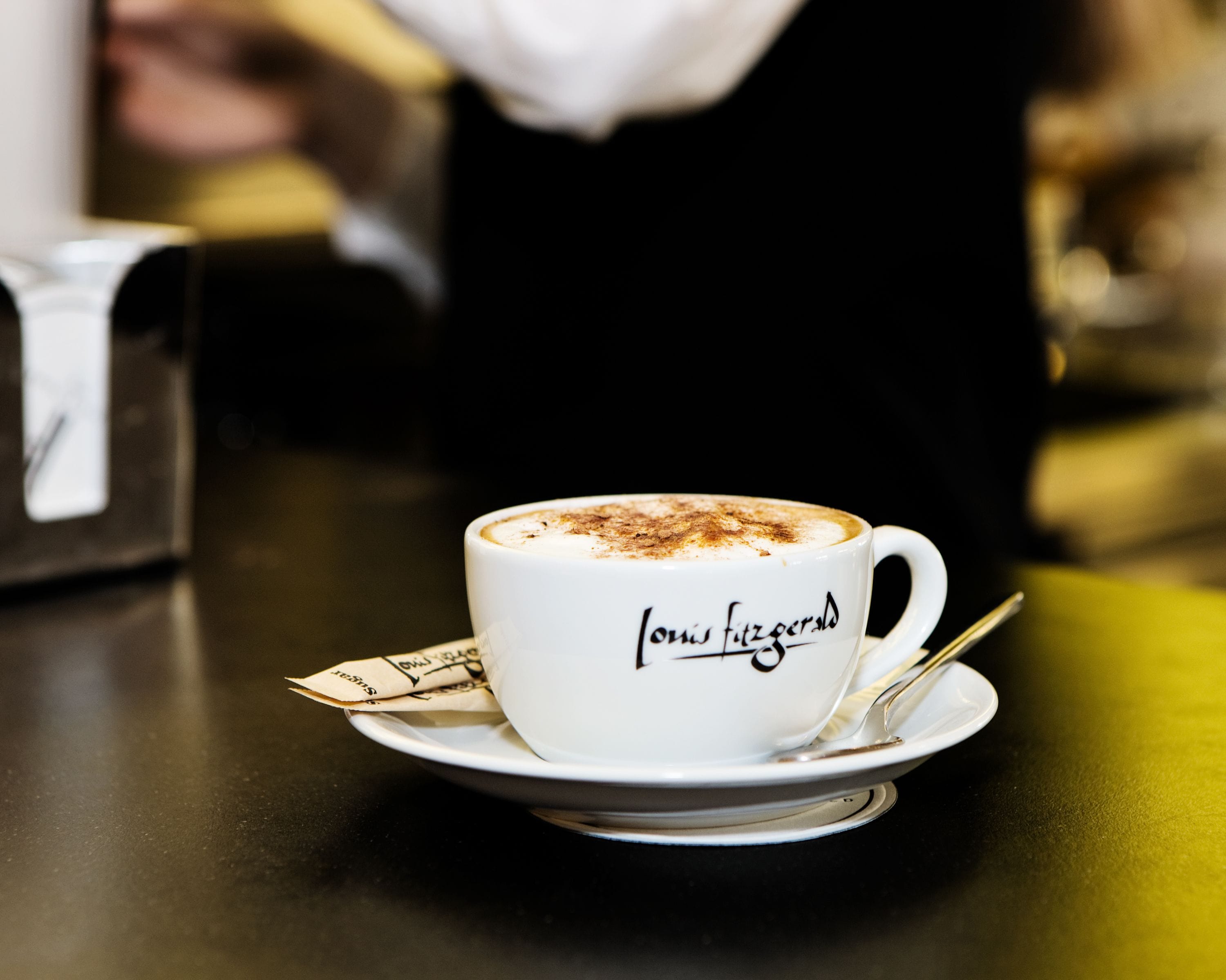 Una taza blanca de café con una cuchara sobre un plato, colocada en una mesa.