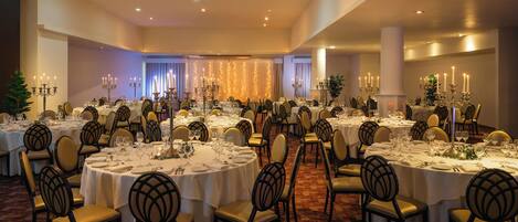 A banquet hall with round tables set for dining, featuring chandeliers and candelabras.