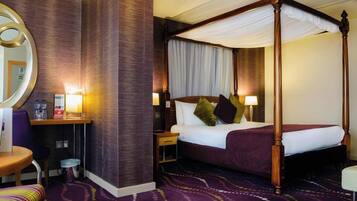 A four-poster canopy bed with a nightstand, a desk with a chair, and a round mirror.