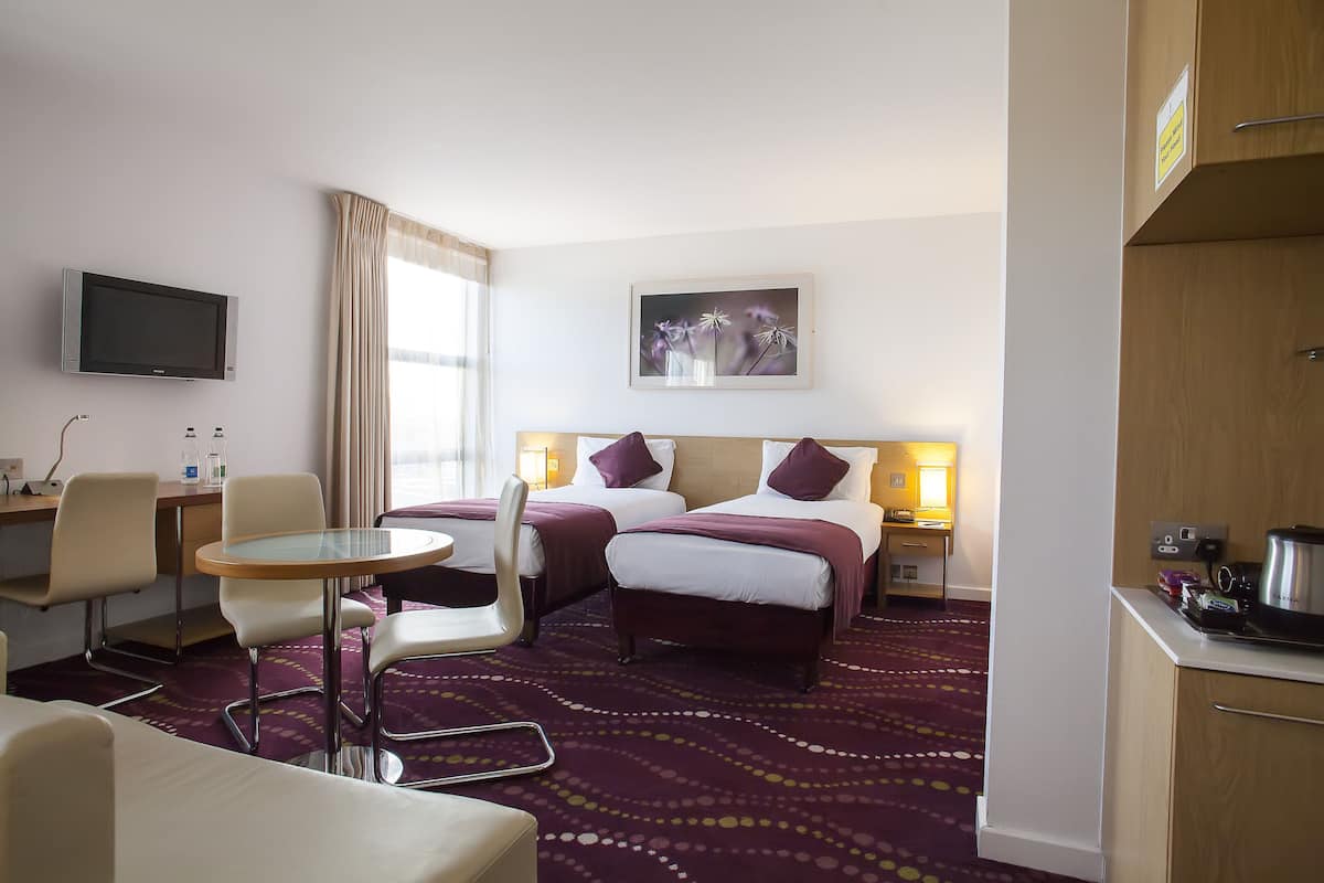 A hotel room with two beds, a TV, a desk, a chair, a small table, and a carpeted floor.