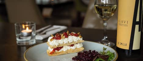 A dessert plate with a pastry, a glass of white wine, a candle, and a bottle of wine on a table.
