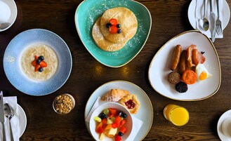 Impostazione colazione con diversi piatti, tra cui pancake, frutta e pasticceria, su un tavolo di legno.