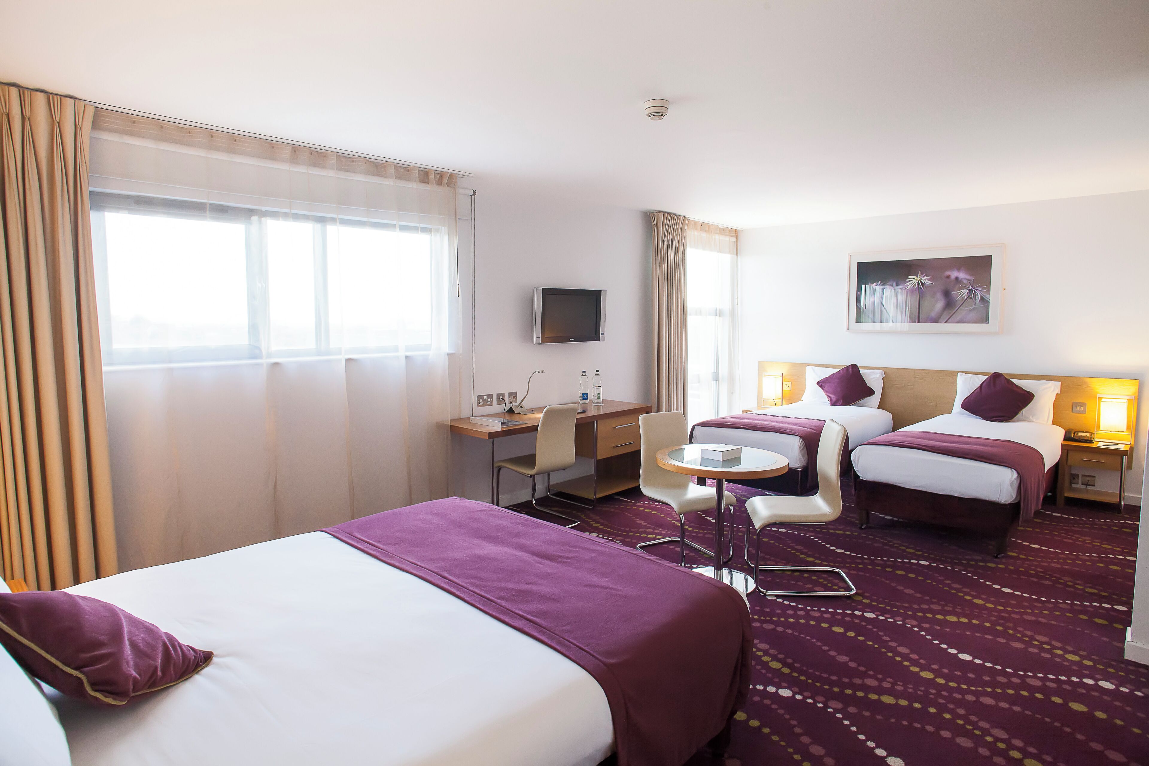 A hotel room with two beds, a desk, a chair, a television, and a window with curtains.