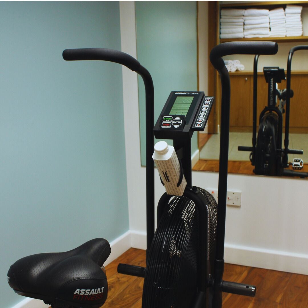 Màquina d'exercici amb pantalla digital, portabotas d'aigua i seient amb la marca "ASSAULT FITNESS".