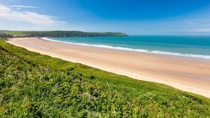 A coastal landscape with a sandy beach, grassy areas, and a clear blue sky. - The Park Hotel (Barnstaple)
