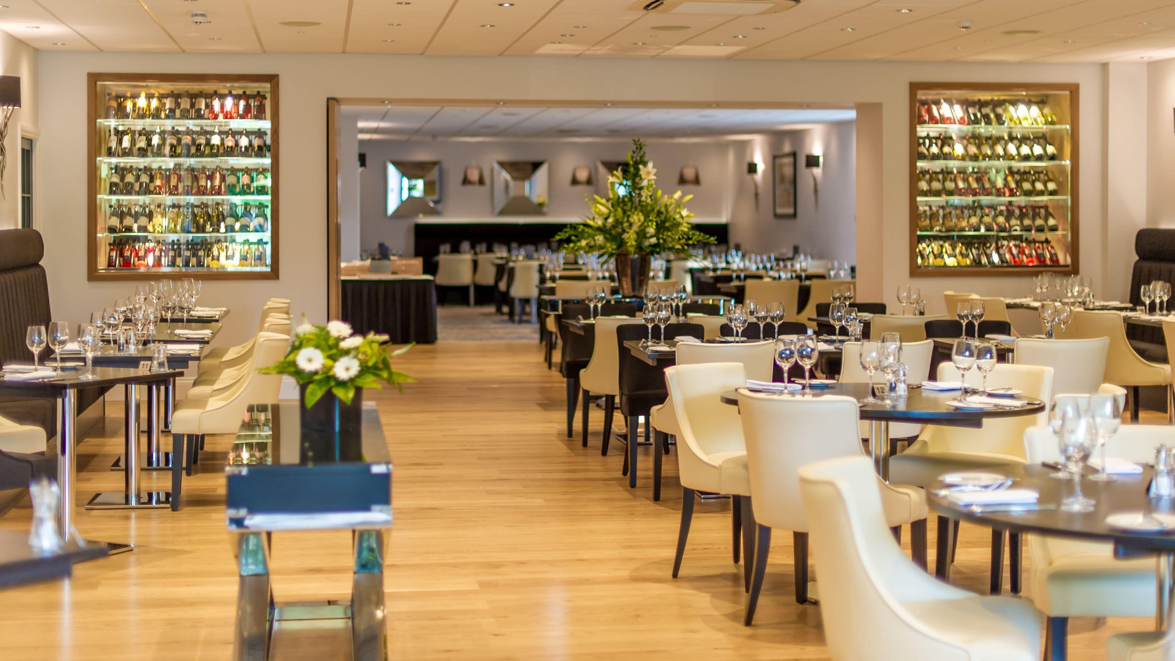A restaurant with tables set for dining, a bar area with bottles, and a large flower arrangement.