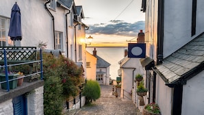 A cobblestone street in a coastal town with white buildings, a view of the sea, and hanging flower baskets. - The Park Hotel (Barnstaple)