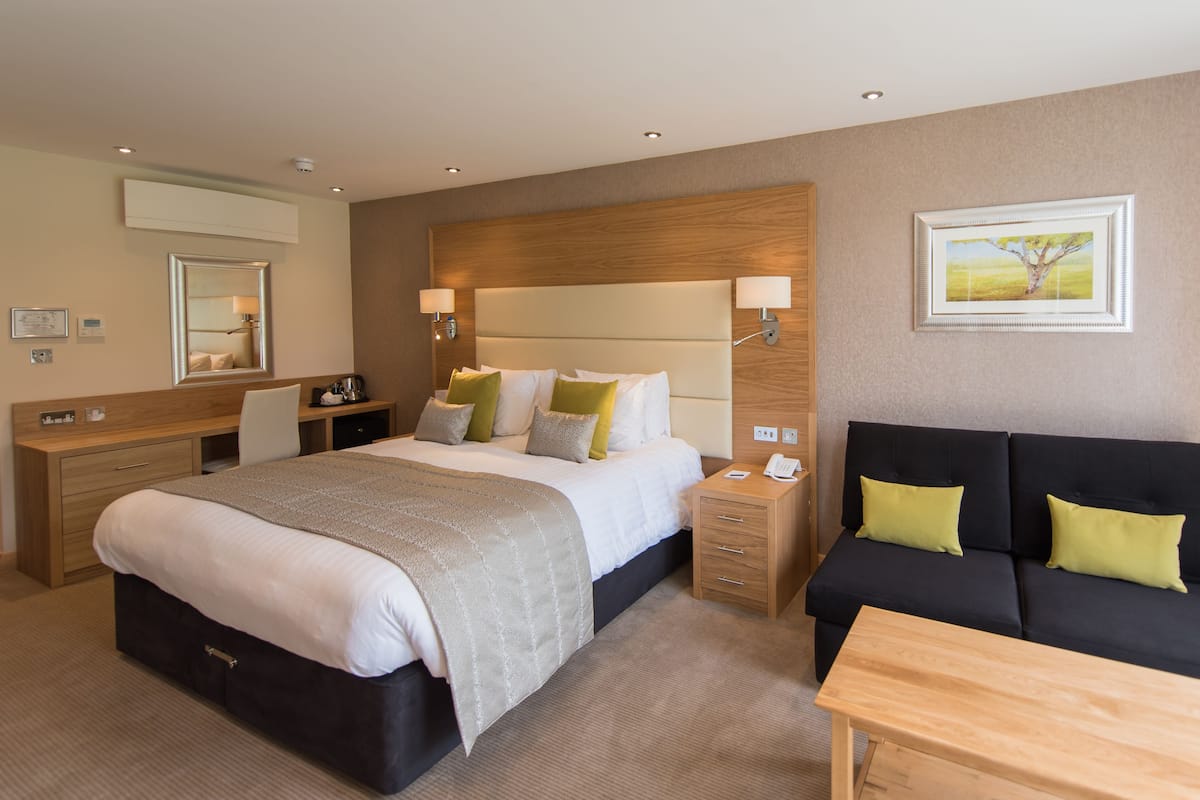 A hotel room with a large bed, a sofa, a desk, and a bedside table.