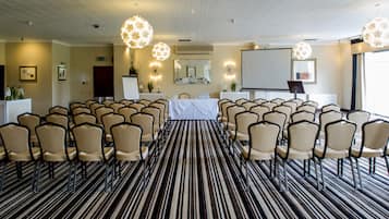A conference room with rows of chairs, a projector screen, and a large mirror.