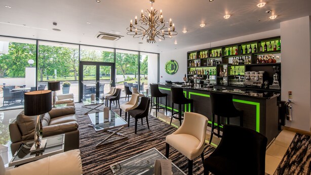 A modern bar area with a green-lit bar counter, various liquor bottles, and a chandelier. - The Park Hotel (Barnstaple)