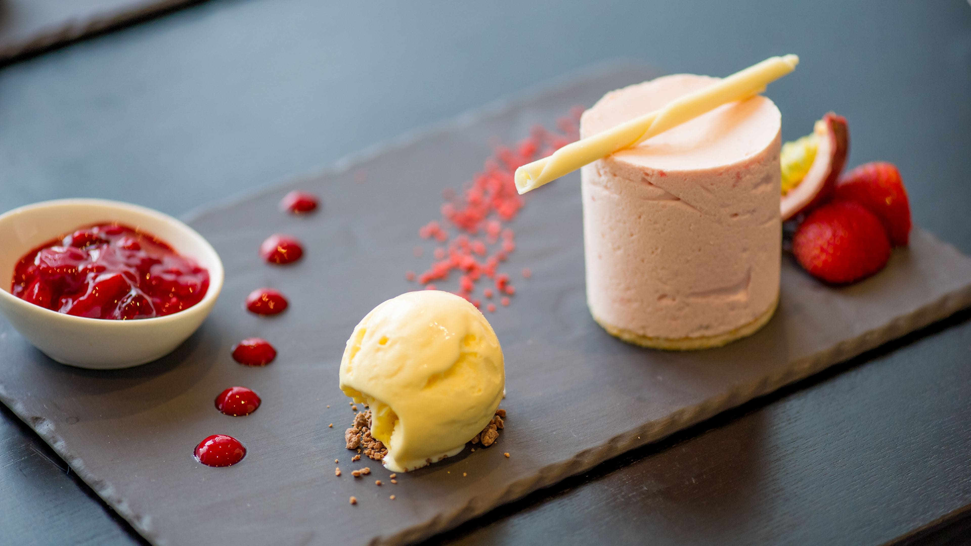 A dessert plate with a scoop of vanilla ice cream, a glass of pink smoothie, and a bowl of red fruit compote.
