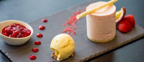 A dessert plate with a scoop of vanilla ice cream, a glass of pink smoothie, and a bowl of red fruit compote.