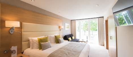 A modern hotel room with a large bed, bedside tables, a seating area, and a view of the outdoors.