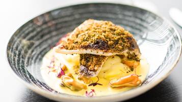 A dish with a crispy breadcrumb topping, served on a plate with a creamy sauce and garnished with purple flowers.