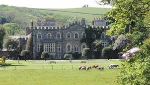 A large stone building with arched windows and a symmetrical facade, surrounded by a well-maintained lawn and grazing cattle. - The Park Hotel (Barnstaple)