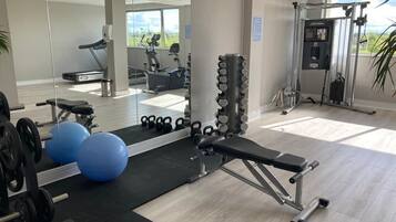 A gym with exercise equipment, mirrors, and a weightlifting area.
