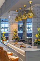 Una zona de bar moderna con encimera de mármol, lámparas colgantes doradas y una variedad de flores.