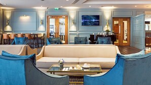 A modern hotel lobby with a beige sofa, blue armchairs, a coffee table with pastries, and a piano. - City North Hotel and Conference Centre (Gormanston)