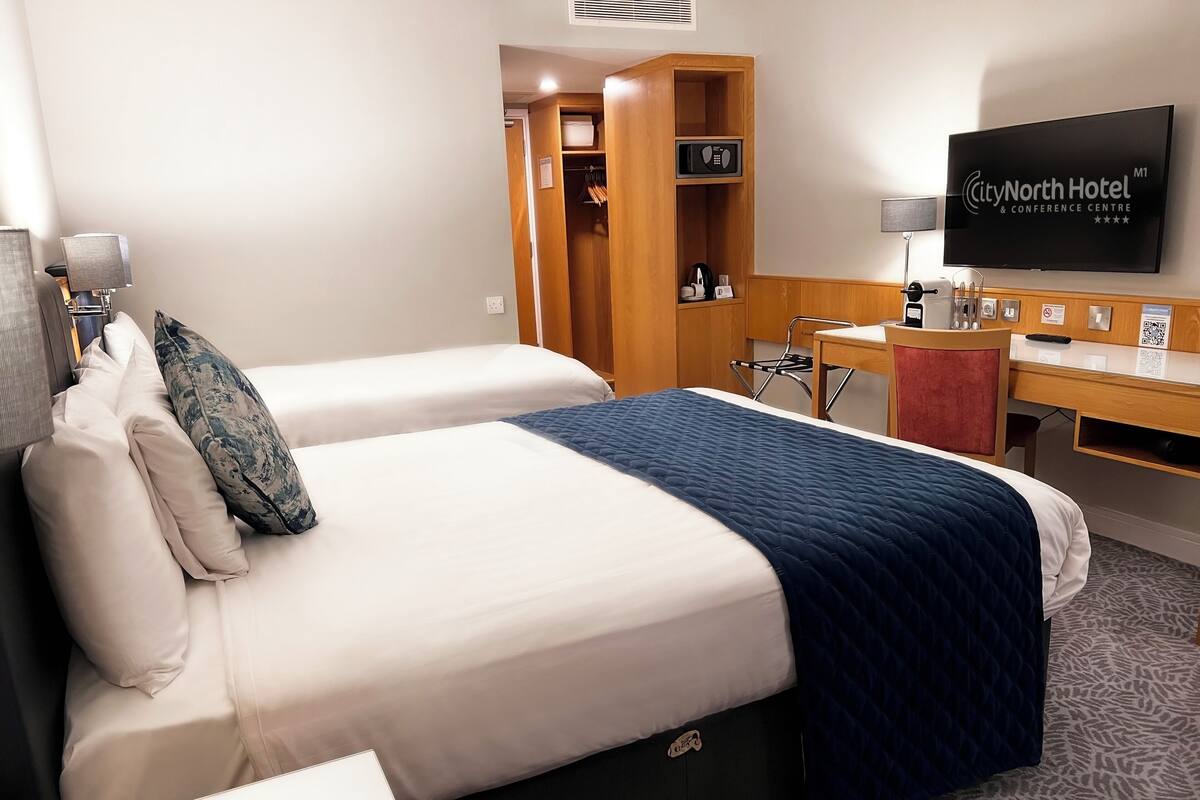 A hotel room with two beds, a desk, a TV, and a wardrobe.