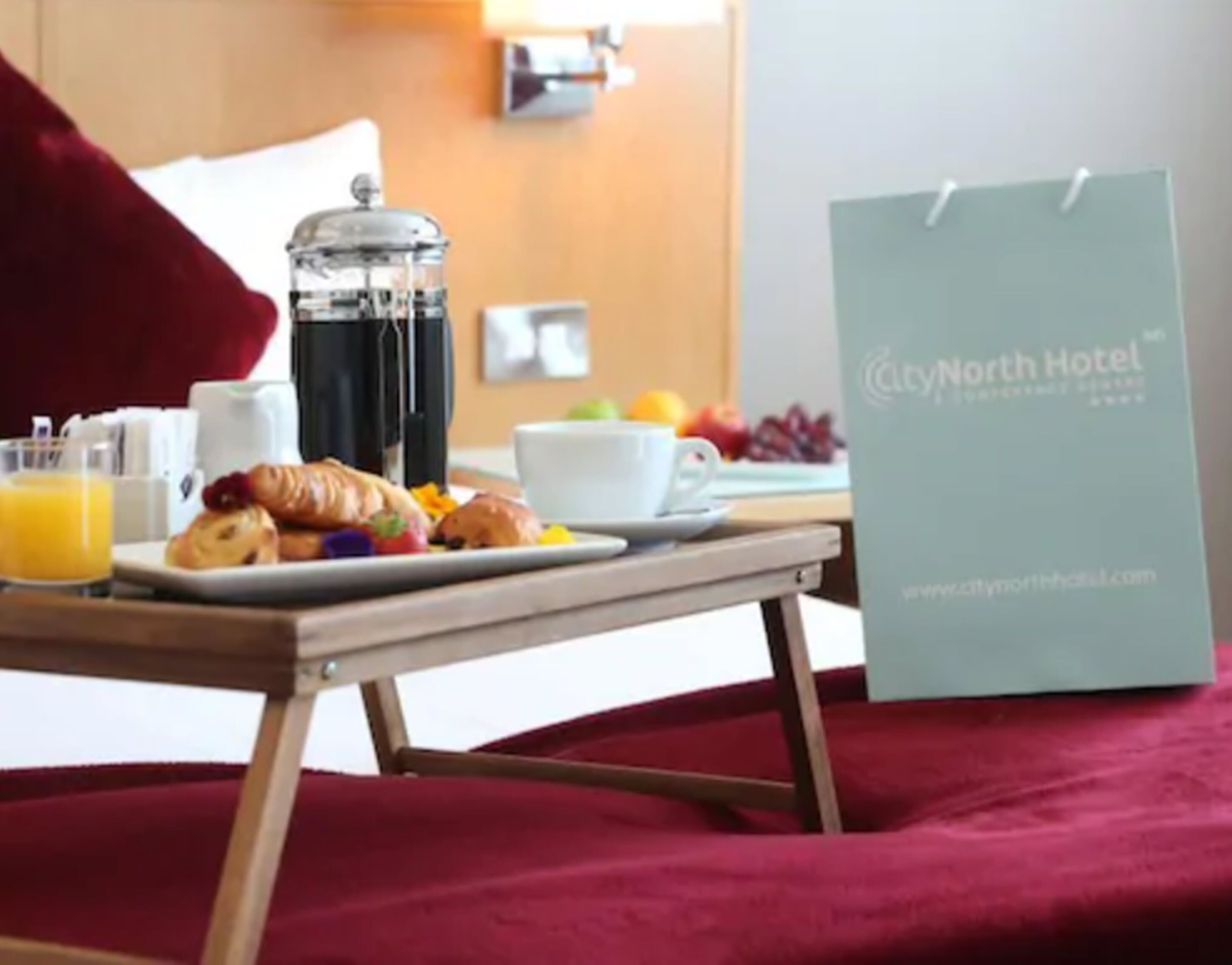 A breakfast setup with croissants, orange juice, and a coffee pot on a table. A City North Hotel sign is visible.