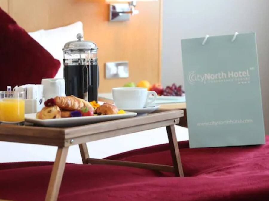 A breakfast setup with croissants, orange juice, and a coffee pot on a table. A City North Hotel sign is visible.