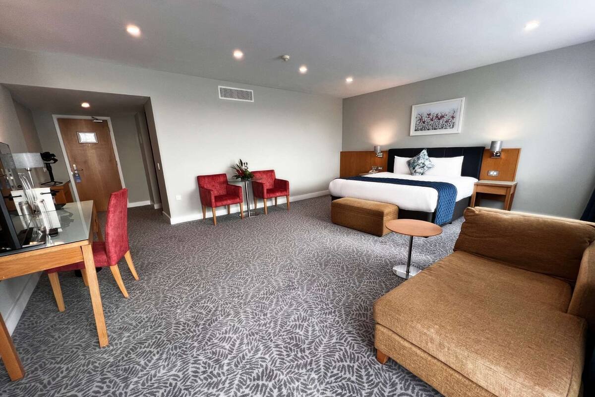 A hotel room with a bed, a desk with a chair, a small table, and a sofa.