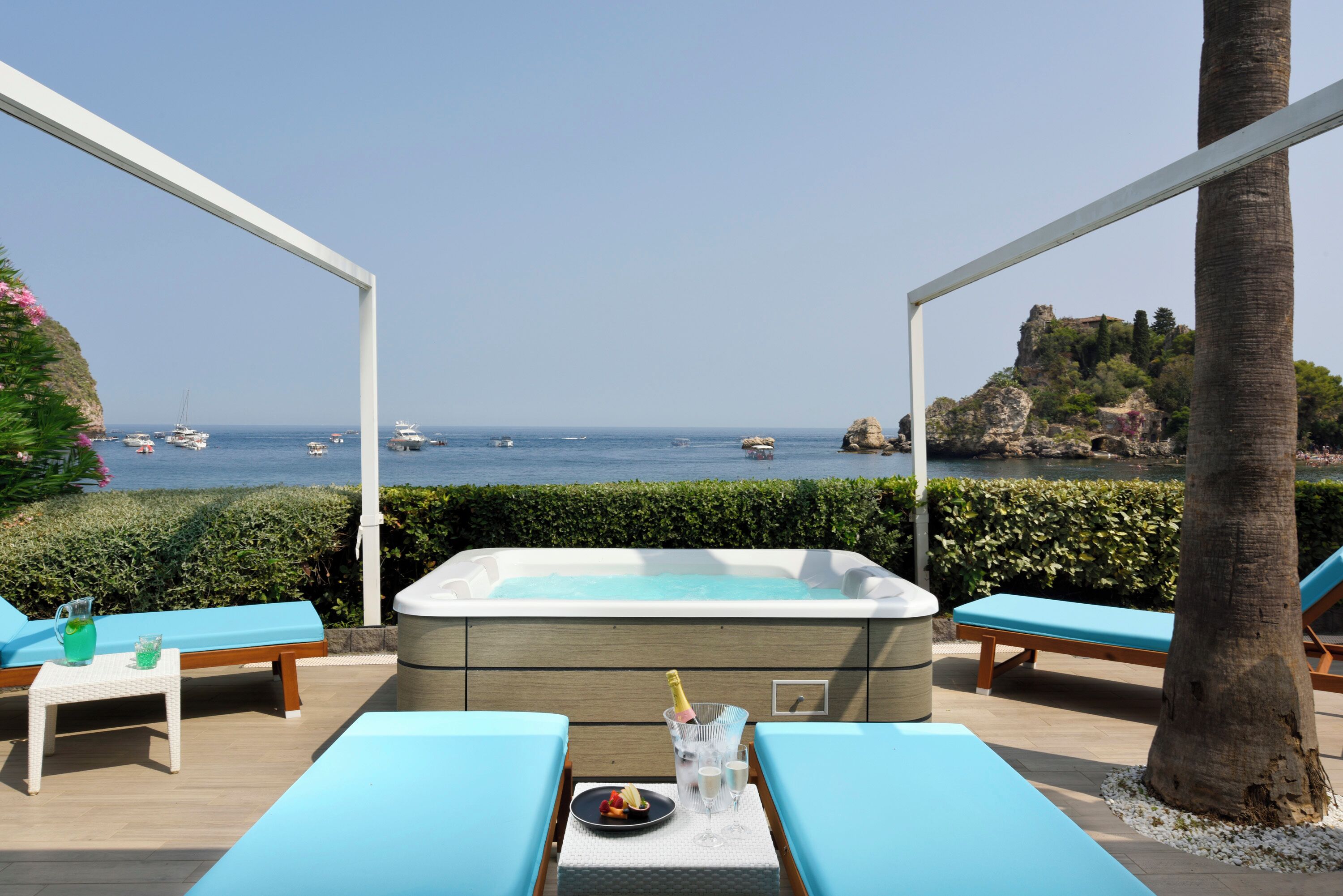 Un área junto a la piscina con un jacuzzi, sillas de descanso y una mesa con bebidas y aperitivos.