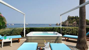 Un área junto a la piscina con un jacuzzi, sillas de descanso y una mesa con bebidas y aperitivos.