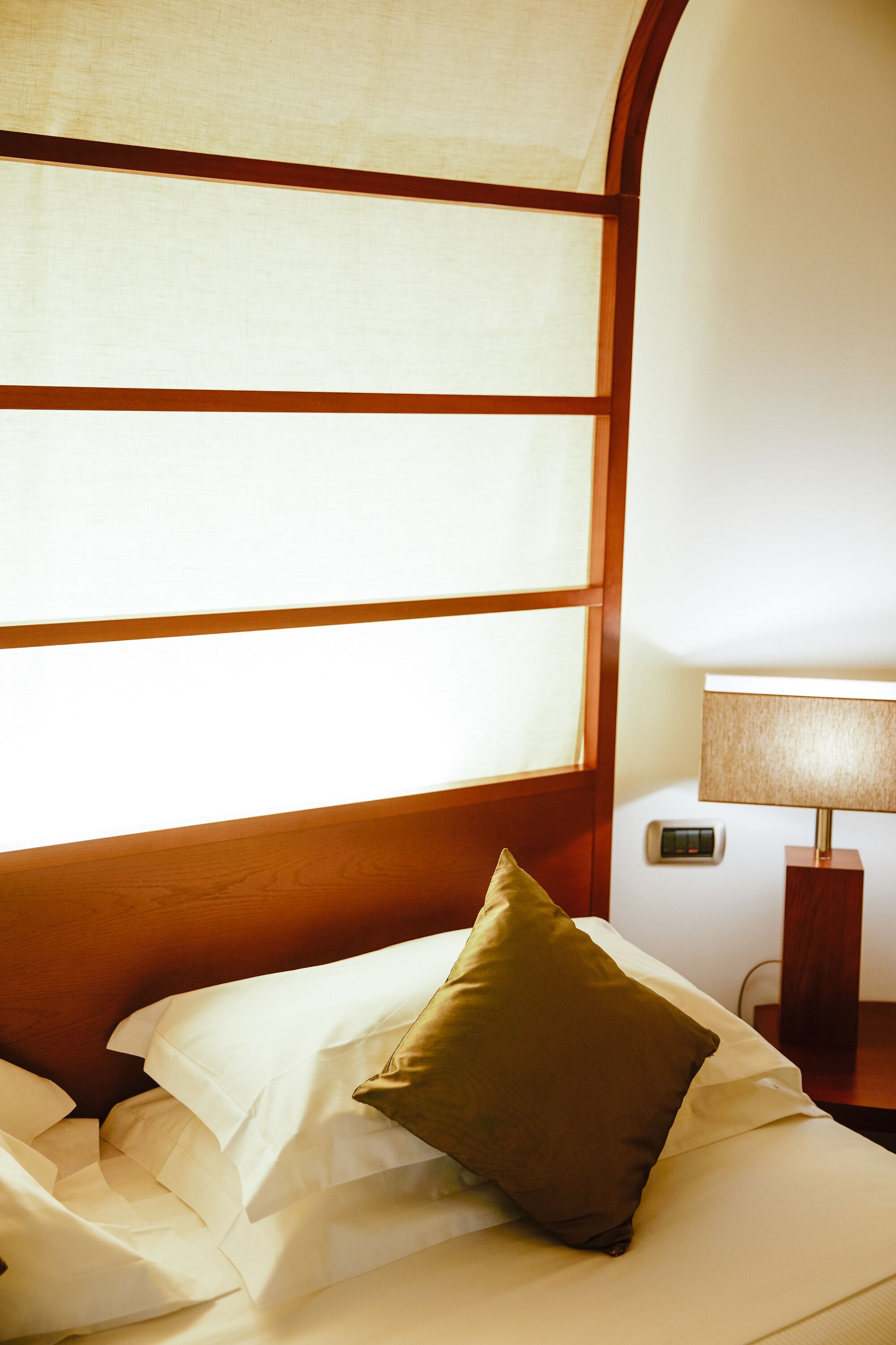 A hotel room with a bed, a nightstand, a lamp, and a window with wooden frames.