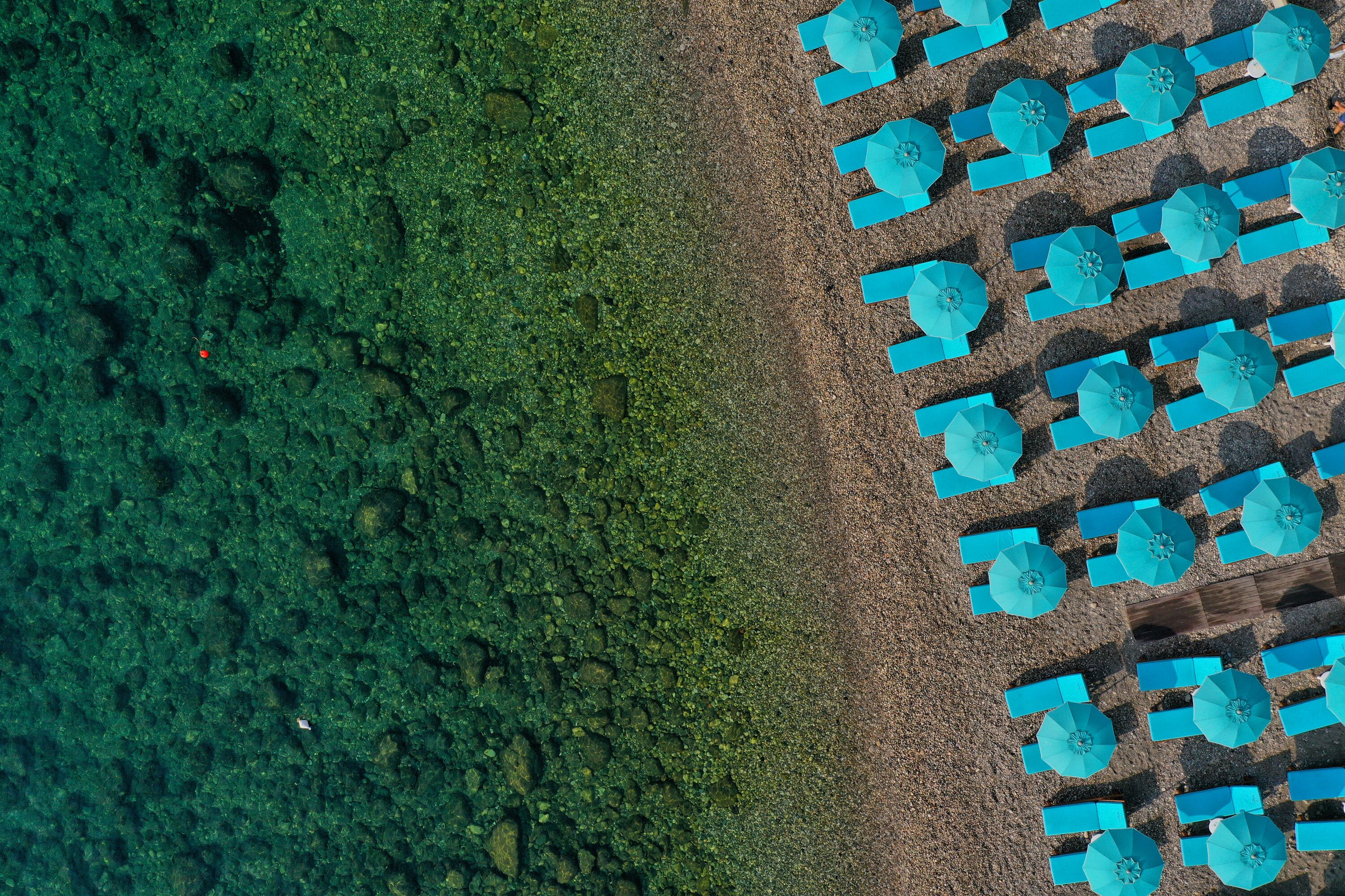 Vista aérea de una playa con numerosos sombrillas azules dispuestas en filas.