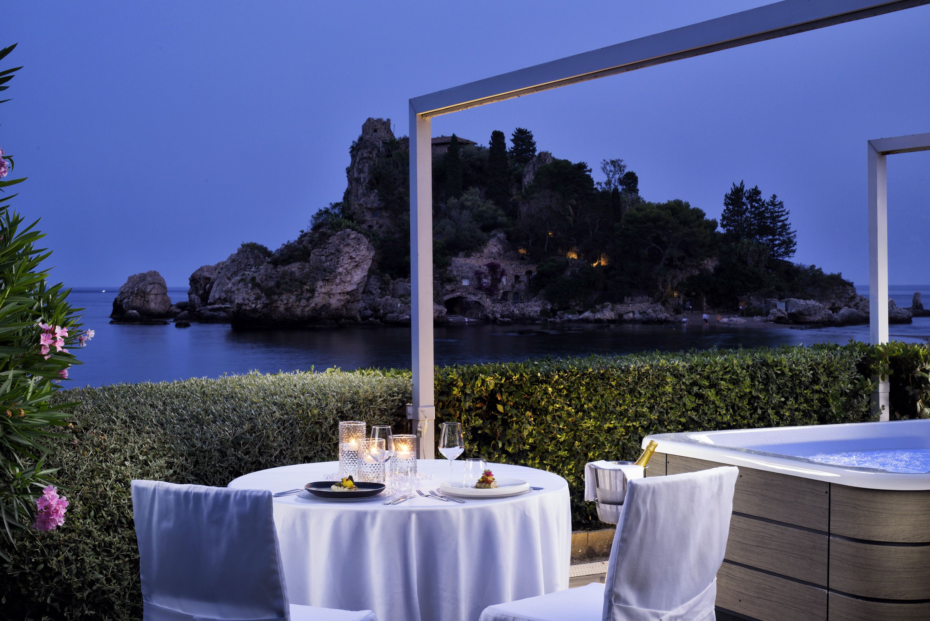 A round table set for dining with a view of a rocky island and the sea.