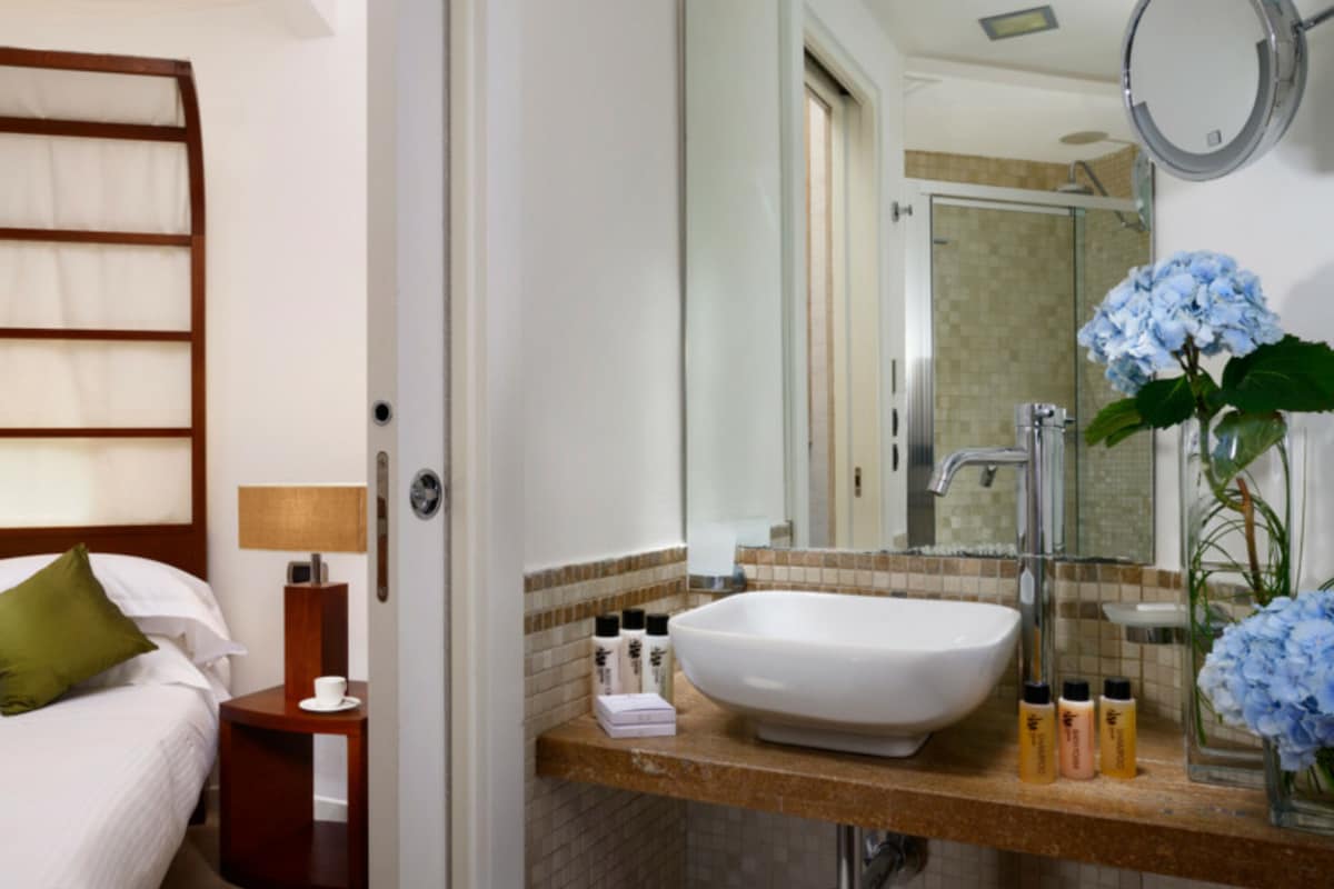 A hotel bathroom with a large sink, a mirror, and toiletries on the counter.