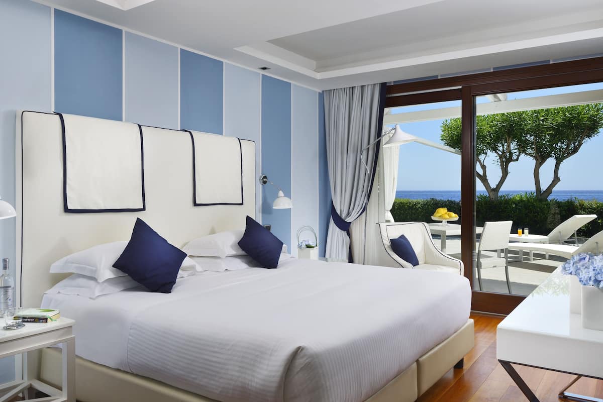 A hotel room with a large bed, a desk, and a view of the sea.