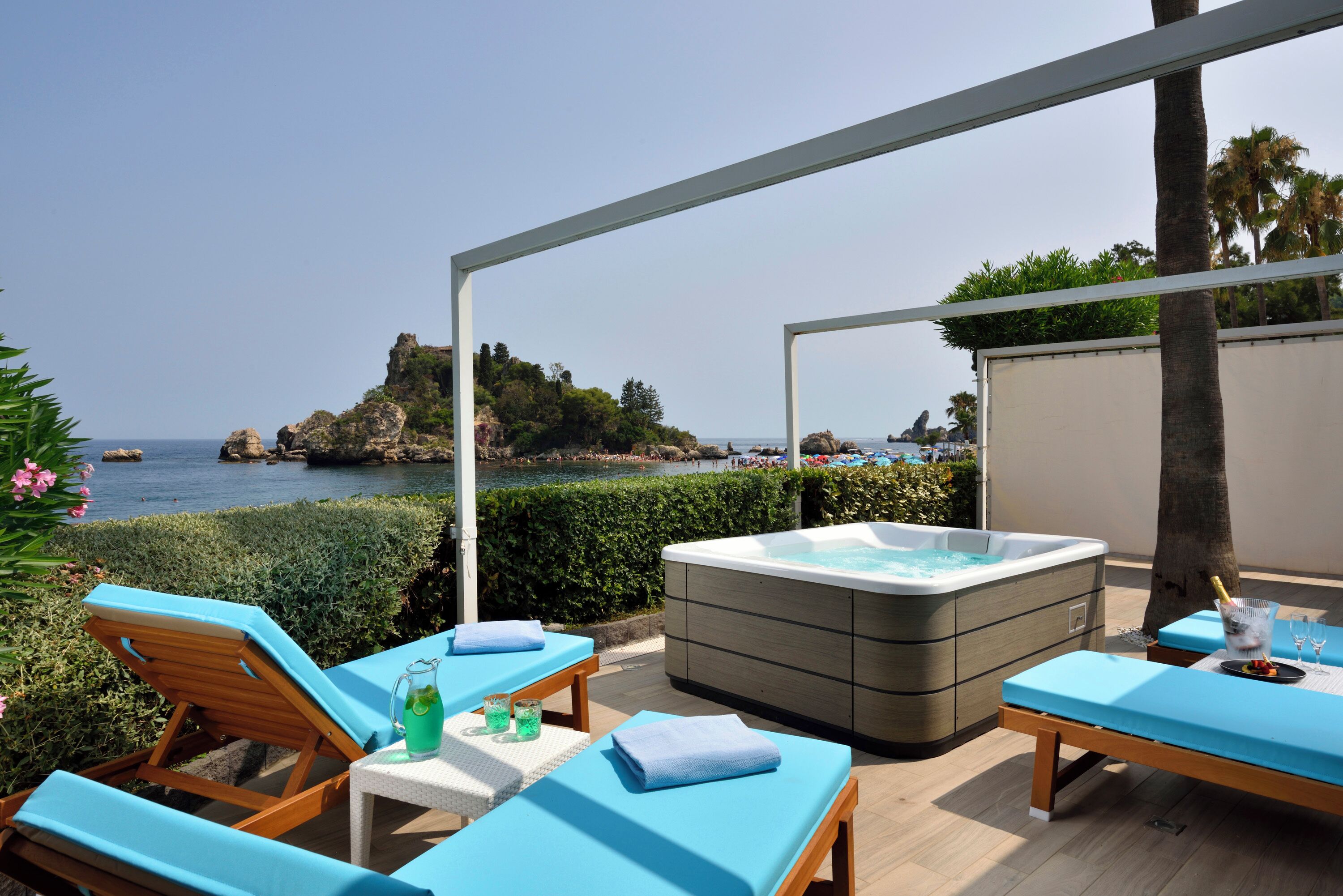 A rooftop terrace with lounge chairs, a hot tub, and a view of the sea and rocky cliffs.