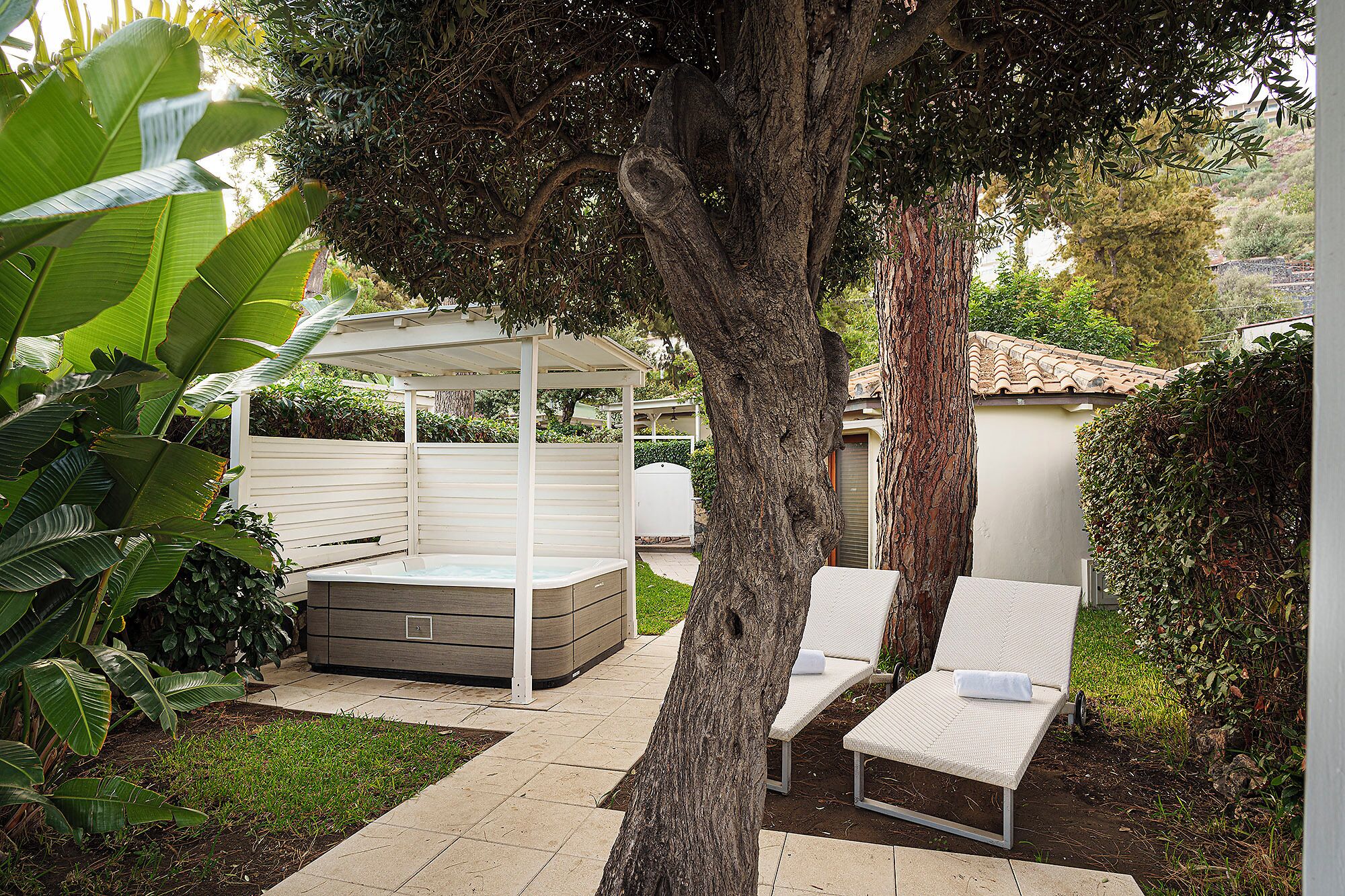 A patio area with a hot tub, two lounge chairs, and a pergola.