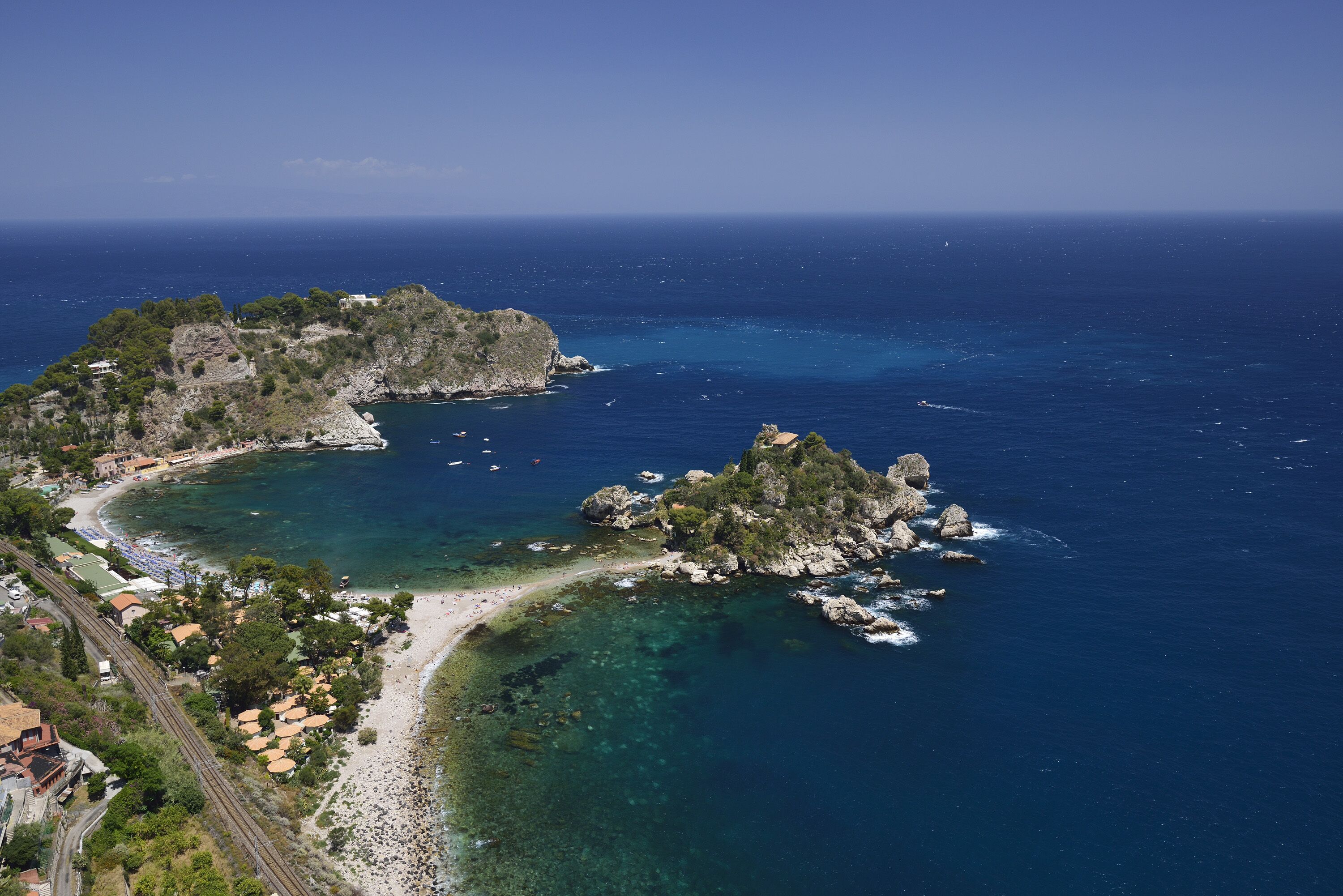 A coastal area with a beach, rocky outcrops, and buildings along the shoreline.